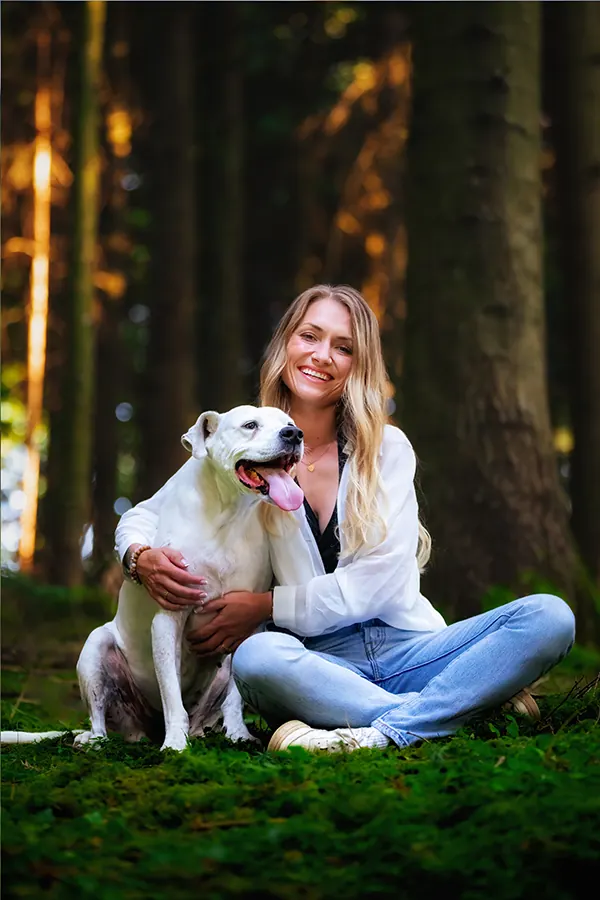 Hundetrainerin Julia Fuchs sitzt mit ihrem weissen Hund im Wald